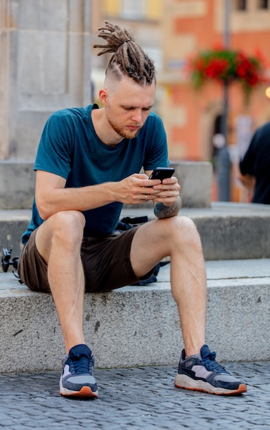 Jonge man met dreadlocks zit met een telefoon op straat