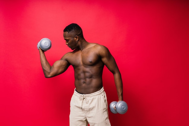 Jonge man met dumbbells goede lichaamsbouw geïsoleerd op rode en zwarte achtergrond kracht en motivatie