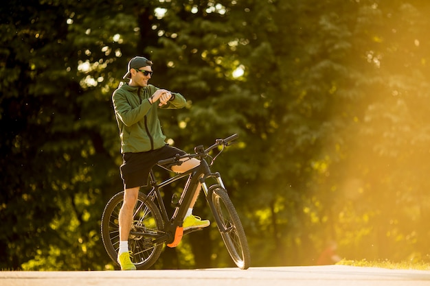 Jonge man met ebike, mountainbike met elektrische batterij, tijd in het park controleren