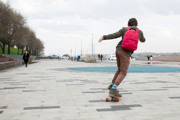 Jonge man met een baard met een rugzak en een longboard op straat