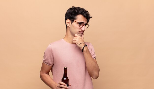 Jonge man met een biertje denken, twijfelachtig en verward, met verschillende opties, zich afvragend welke beslissing hij moet nemen