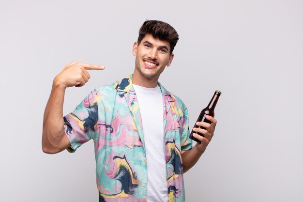 Jonge man met een biertje glimlachend vol vertrouwen wijzend naar eigen brede glimlach, positieve, ontspannen, tevreden houding