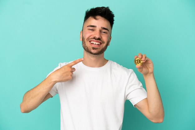 Jonge man met een Bitcoin geïsoleerd op een blauwe achtergrond met een duim omhoog gebaar