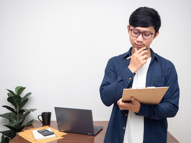 Jonge man met een bril staat op de werkplek en controleert document in de hand