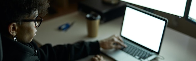 Foto jonge man met een bril zit aan tafel voor veel computermonitoren en gebruikt een laptop