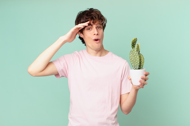 Jonge man met een cactus die er blij, verbaasd en verrast uitziet