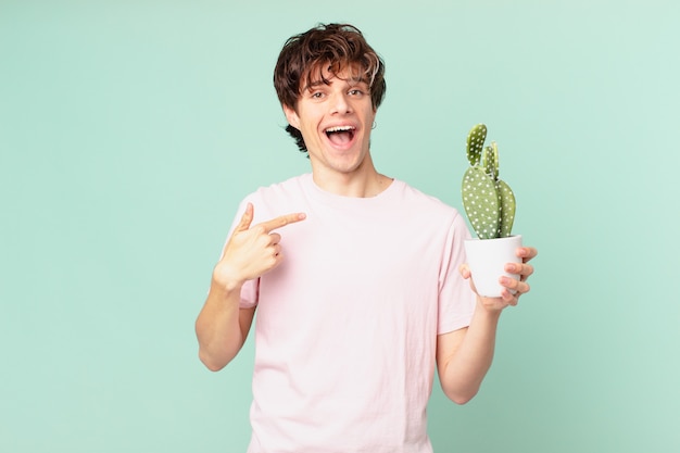 Jonge man met een cactus die zich gelukkig voelt en opgewonden naar zichzelf wijst