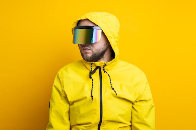 Jonge man met een cyberpunkbril in een gele jas die wegkijkt op een gele achtergrond