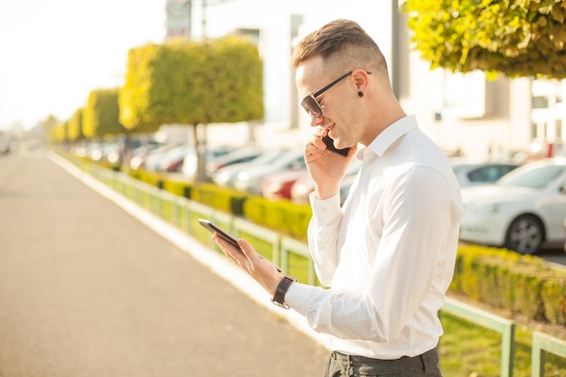 Jonge man met een digitale tablet die op een smartphone praat terwijl hij in de stad staat