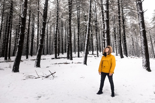 Jonge man met een gele anowak poseren in het midden van een besneeuwd bos