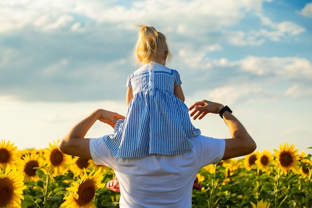 Jonge man met een kind op zijn schouders in een zonnebloem veld.