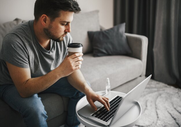 Jonge man met een kopje koffie en met behulp van laptop