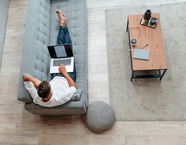 Jonge man met een laptop rust op de bank