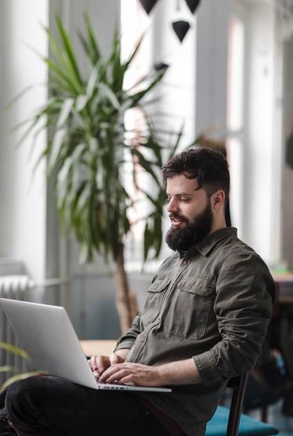 Jonge man met een laptop terwijl hij op een stoel zit