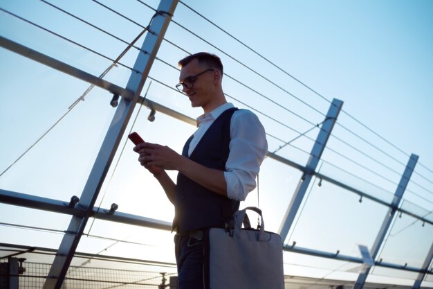 Jonge man met een laptoptas die een bericht leest op zijn smartphone