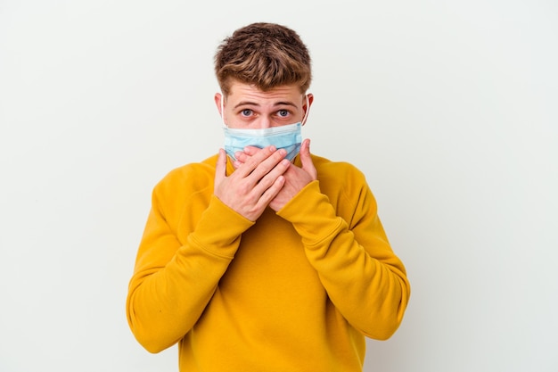 Jonge man met een masker voor coronavirus geïsoleerd op een witte muur geschokt die mond bedekt met handen.