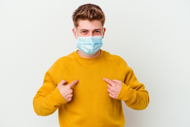 Jonge man met een masker voor coronavirus geïsoleerd op een witte muur verrast wijzend met de vinger.