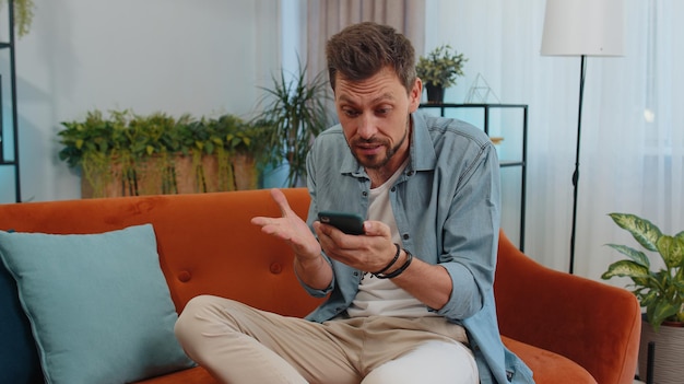 Jonge man met een mobiele telefoon terwijl hij thuis op de bank zit