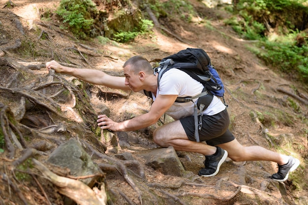 Jonge man met een rugzak klimt op een rotsachtige weg met wortels