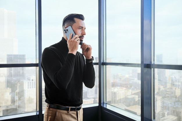 Jonge man met een smartphone die bij het raam staat