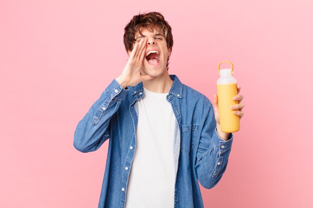 Jonge man met een smoothy gevoel gelukkig, een grote schreeuw gevend met de handen naast de mond