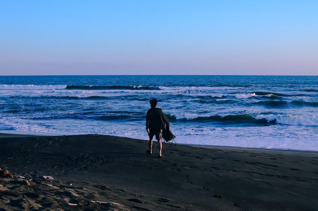 Jonge man met een stoel op het strand kijkend naar de zonsondergang