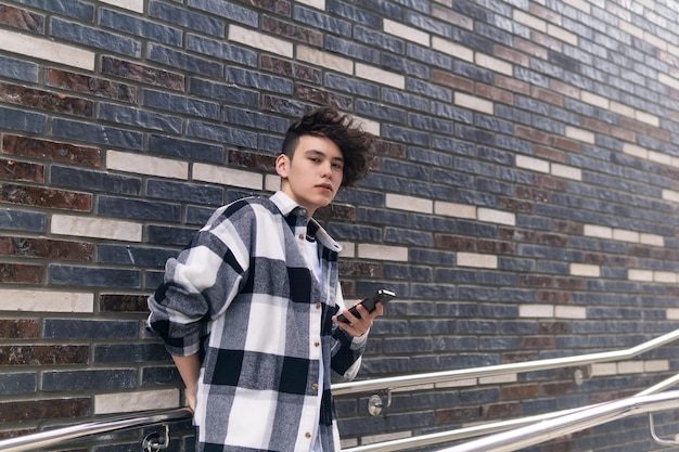 Jonge man met een telefoon tegen een bakstenen muur