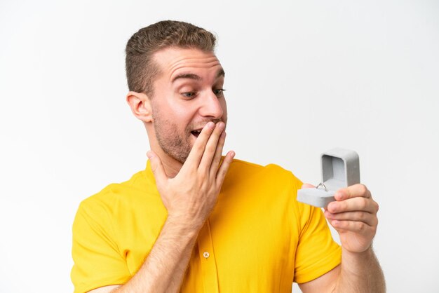 Jonge man met een verlovingsring geïsoleerd op een witte achtergrond met verbazing en geschokte gezichtsuitdrukking