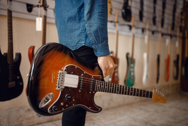 Jonge man met elektrische gitaar in muziekwinkel.