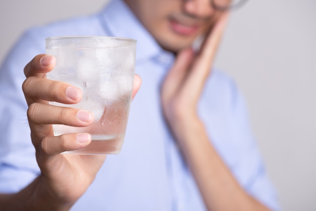 Jonge man met gevoelige tanden en hand met glas koud water met ijs