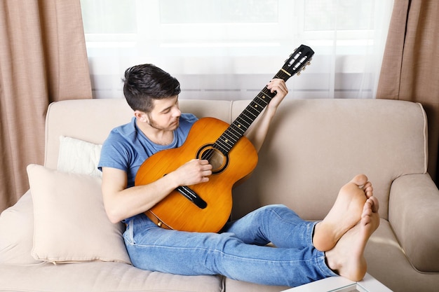Jonge man met gitaar op sofa in de kamer