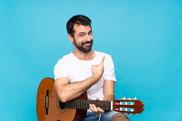 Jonge man met gitaar over geïsoleerde blauw terug te wijzen