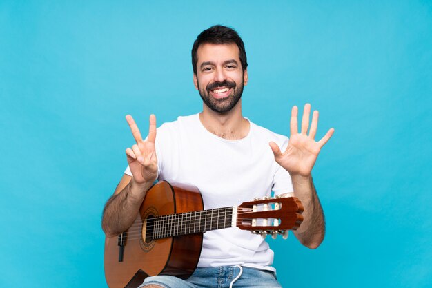 Jonge man met gitaar over geïsoleerde blauw zeven met vingers tellen