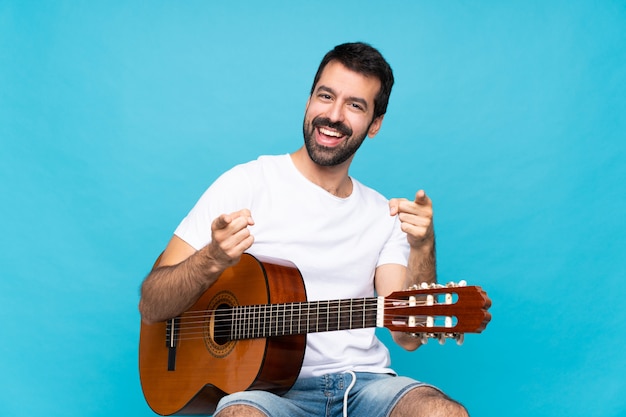 Jonge man met gitaar over geïsoleerde blauwe puntenvinger op je terwijl het glimlachen