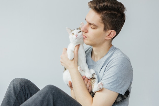 Jonge man met kat op lichtgrijze achtergrond. Favoriete huisdier. Man met kat