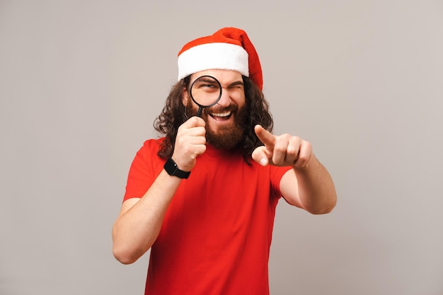 Jonge man met kerstmuts kijkt en wijst naar je door vergrootglas