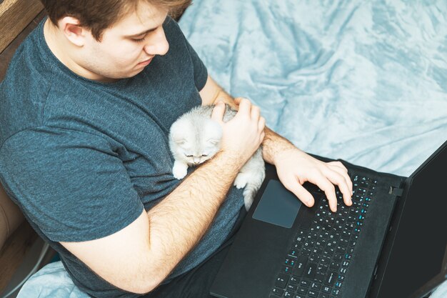 Jonge man met kitten werkt op zijn laptop. Het concept van online leren en werken.