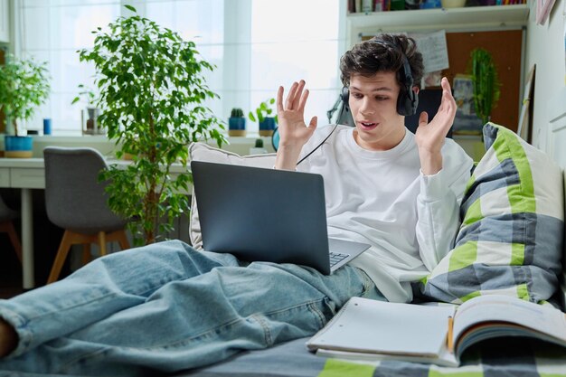 Jonge man met koptelefoon die laptop gebruikt voor videocommunicatie die thuis ligt