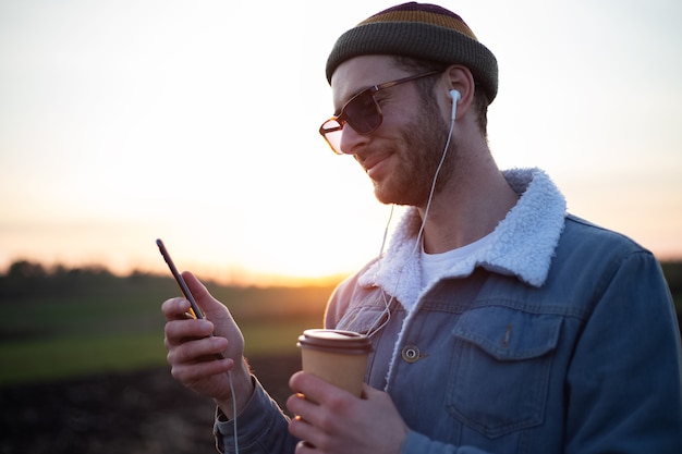 Jonge man met koptelefoon selfies nemen op smartphone met kopje koffie in zijn hand