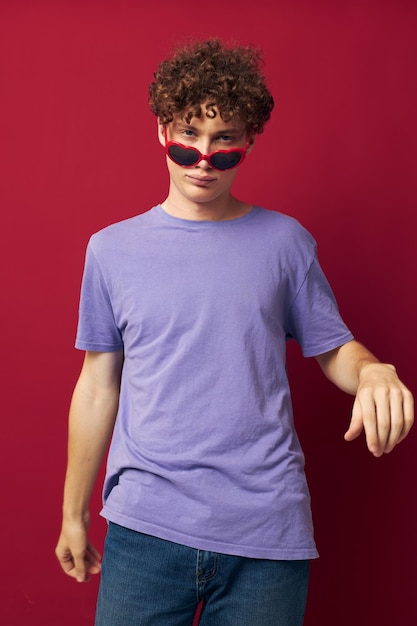 Jonge man met krullend haar handgebaren hartvormige bril poseren geïsoleerde achtergrond