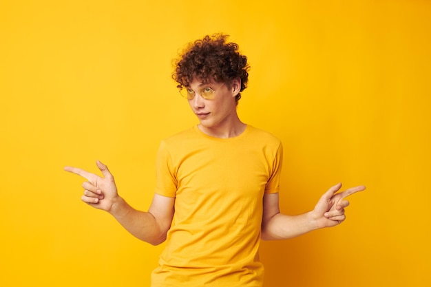 Jonge man met krullend haar met een stijlvolle bril gele t-shirt poseren geïsoleerde achtergrond ongewijzigd