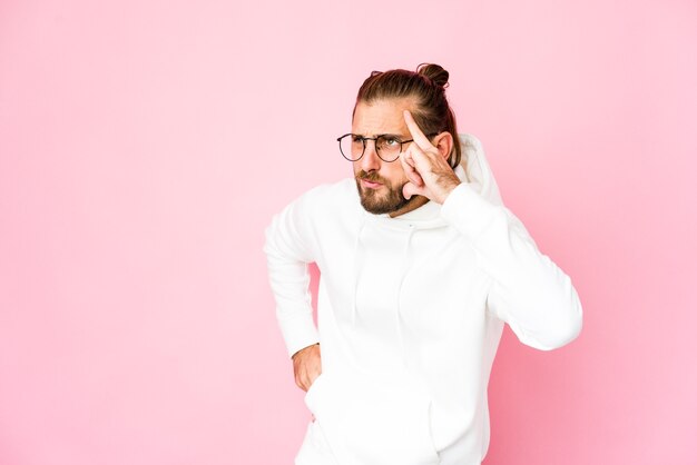 Jonge man met lang haar kijkt tempel met vinger, denken, gericht op een taak.