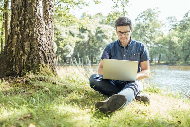 Jonge man met laptop buiten zitten op het gras