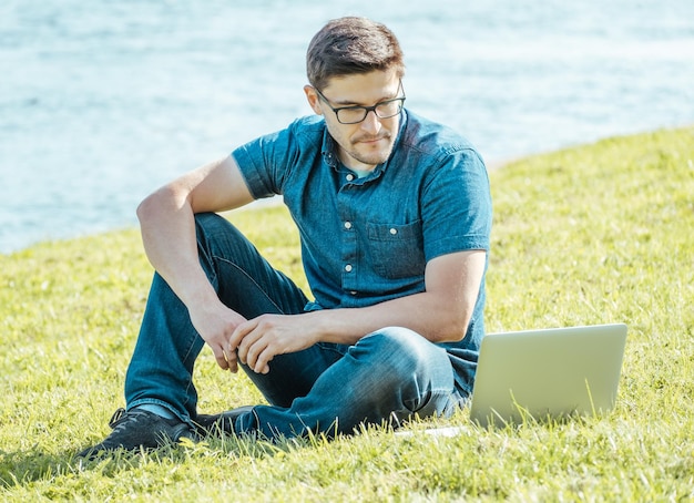 Jonge man met laptop buiten zittend op het gras