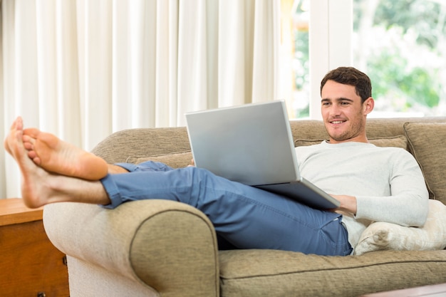 Jonge man met laptop op sofa in de woonkamer