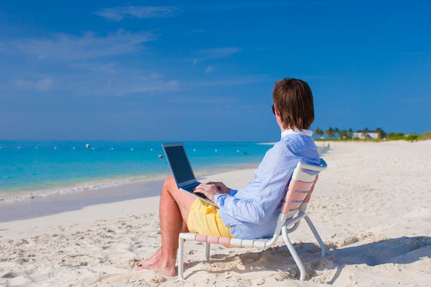 Jonge man met laptop op tropisch strand