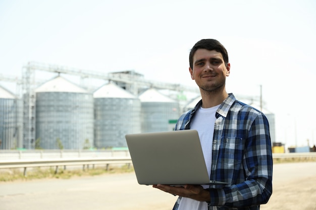 Jonge man met laptop tegen graansilo's. Landbouwbedrijf