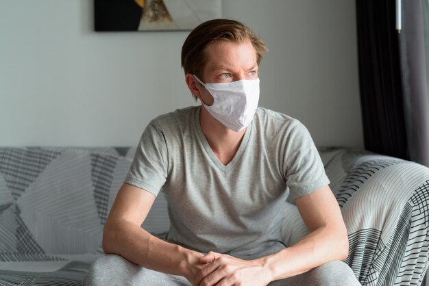 Jonge man met masker denken en thuis blijven in quarantaine