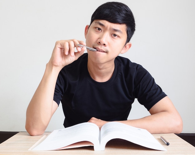 Jonge man met pen denkt en serieus gezicht met het boek op het bureau kijkt naar de camera Studieboekconcept