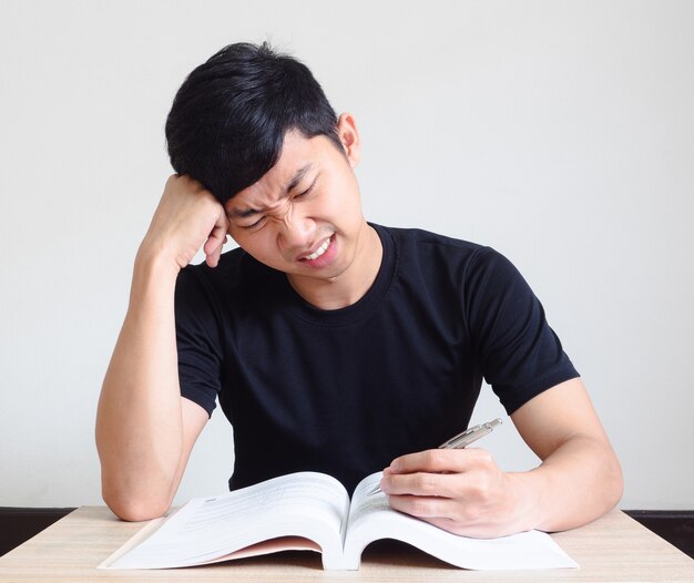 Jonge man met pen serieus en voel spanning met probleem, raak zijn hoofd aan met het boek op het bureau